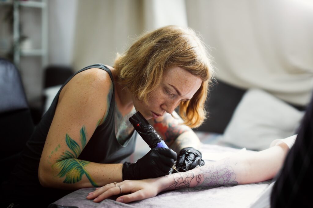 Tattoo parlor, pretty European red-haired girl makes a tattoo on arm.